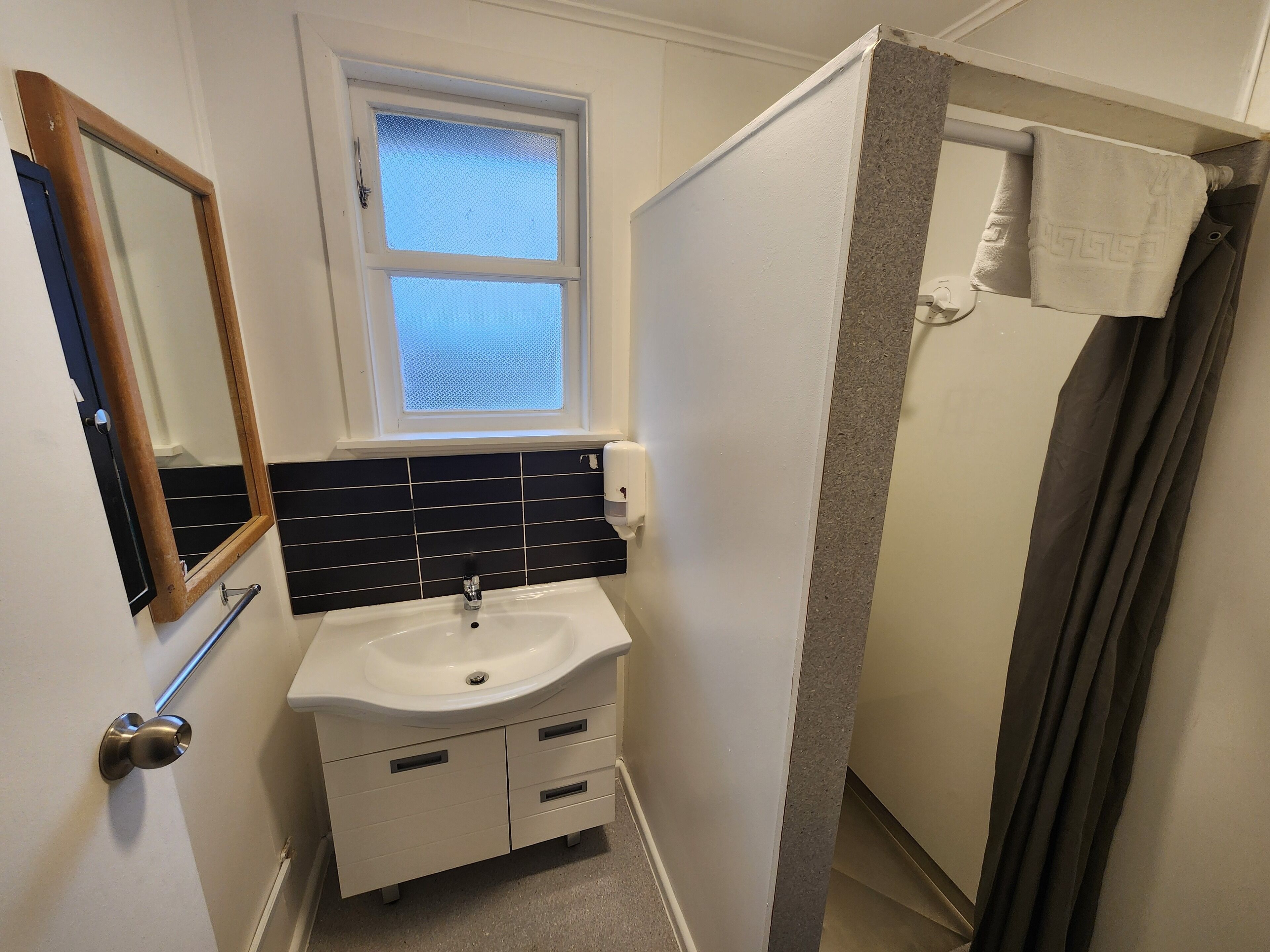 A bathroom with a white sink, black tiled backsplash, a window, and a shower curtain.