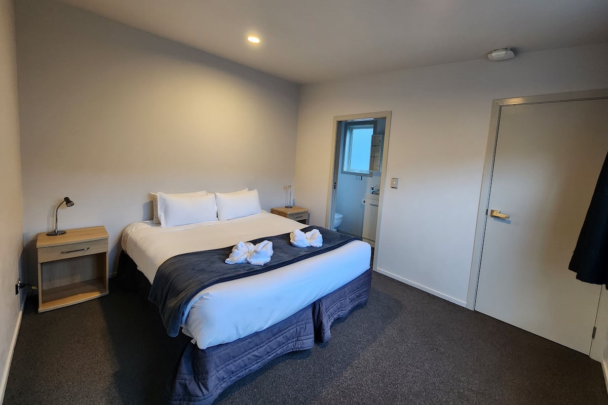 A hotel room with a bed, bedside tables, a wardrobe, and a bathroom visible through an open door.
