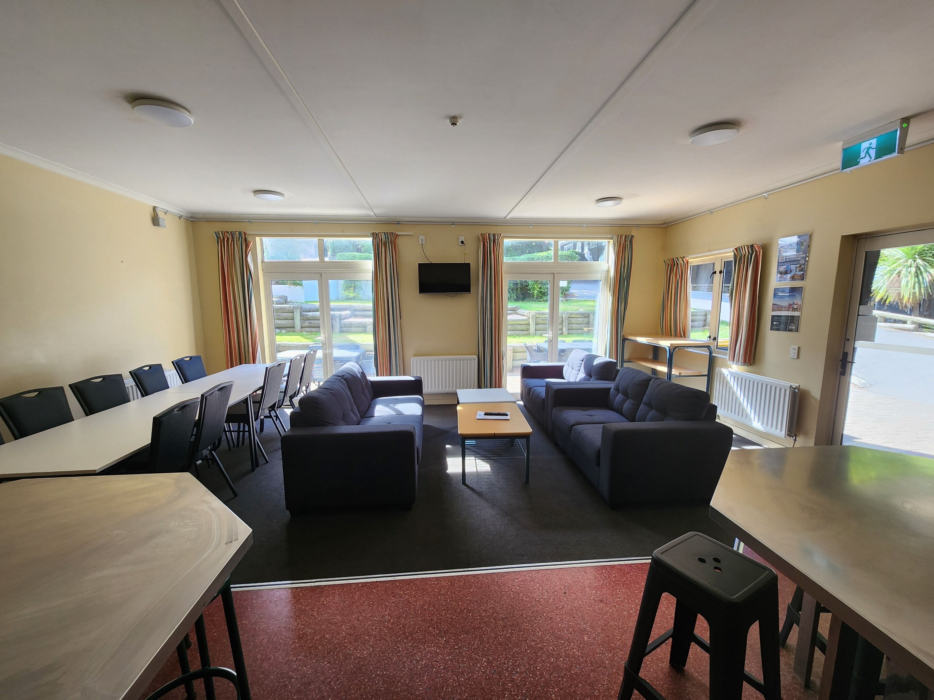 Camera d'albergo con angolo ristoro, due divani, televisore e finestra con tende.