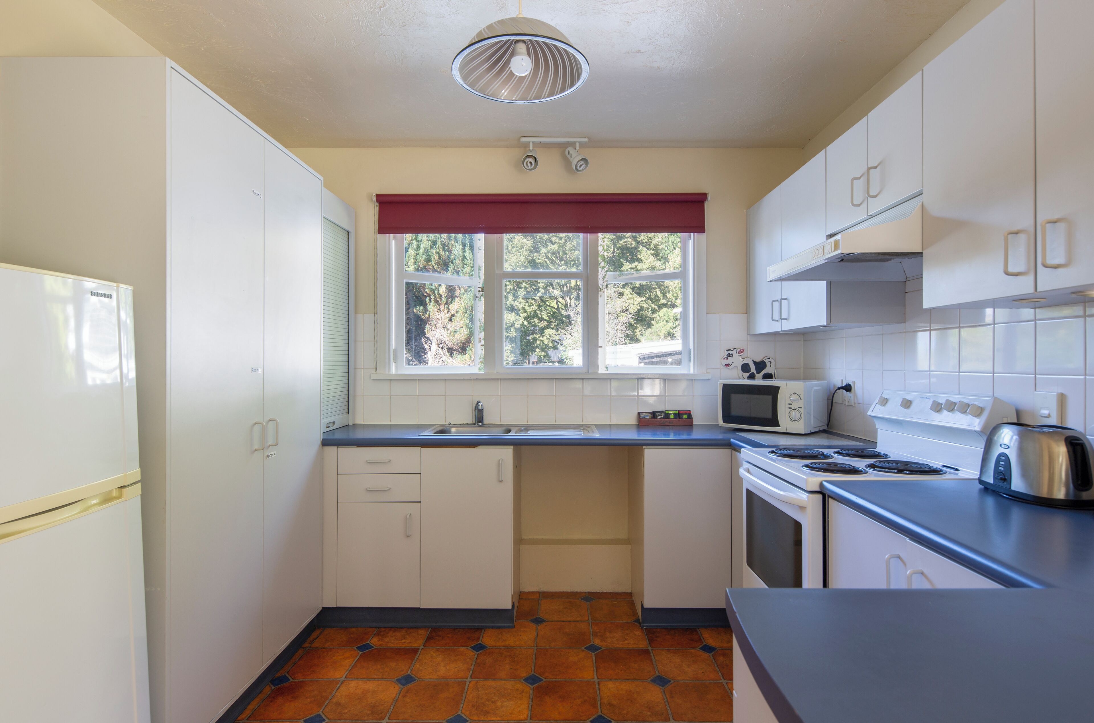 A compact kitchen with white cabinets, a stove, a microwave, and a toaster.