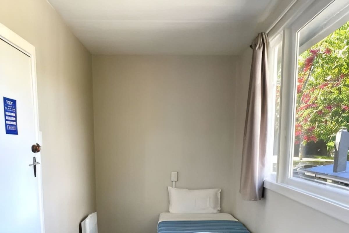A small, compact room with two beds, a window with curtains, and a door with a sign.