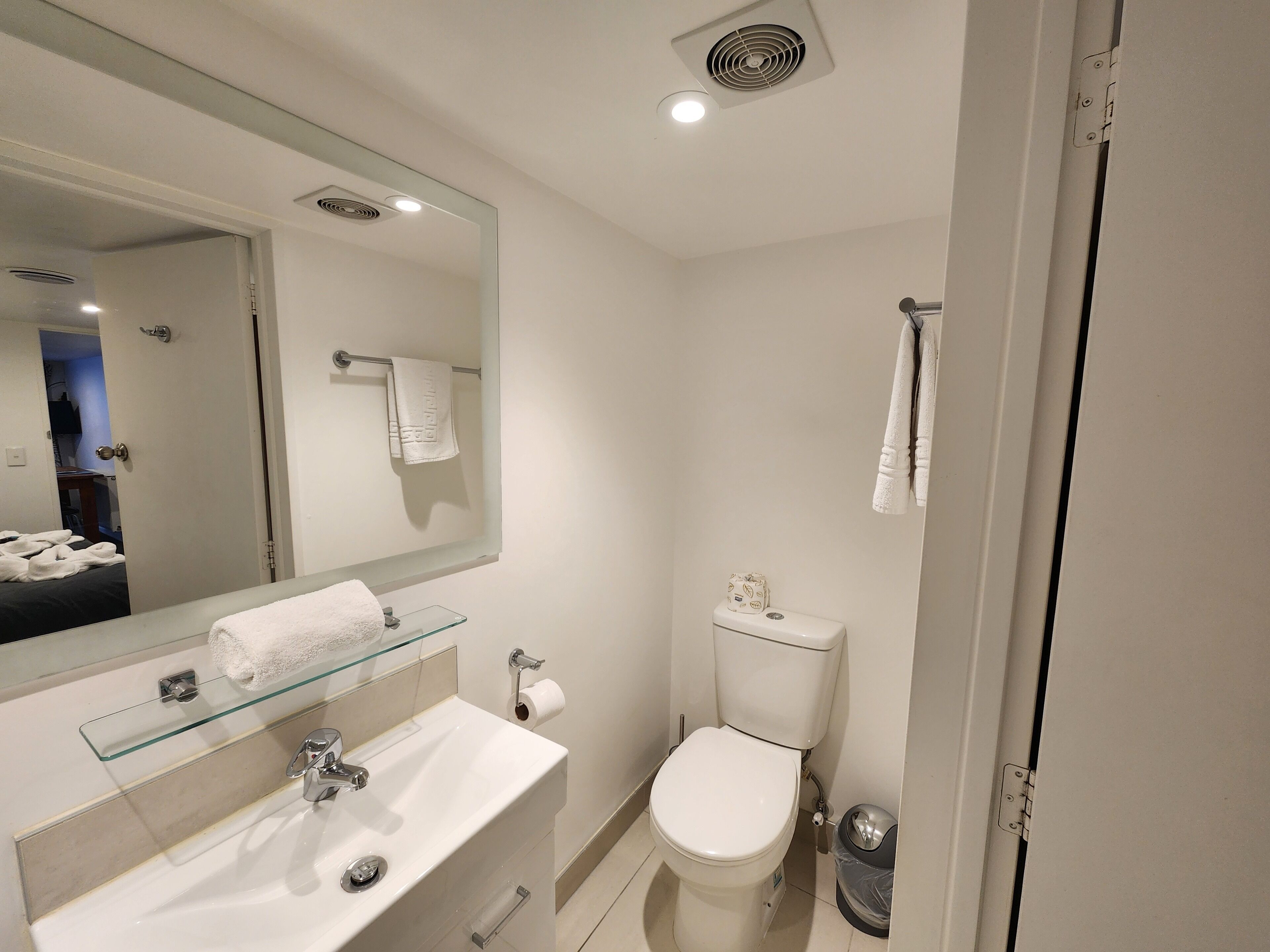 A modern bathroom with a glass-topped sink, a toilet, and a mirror.