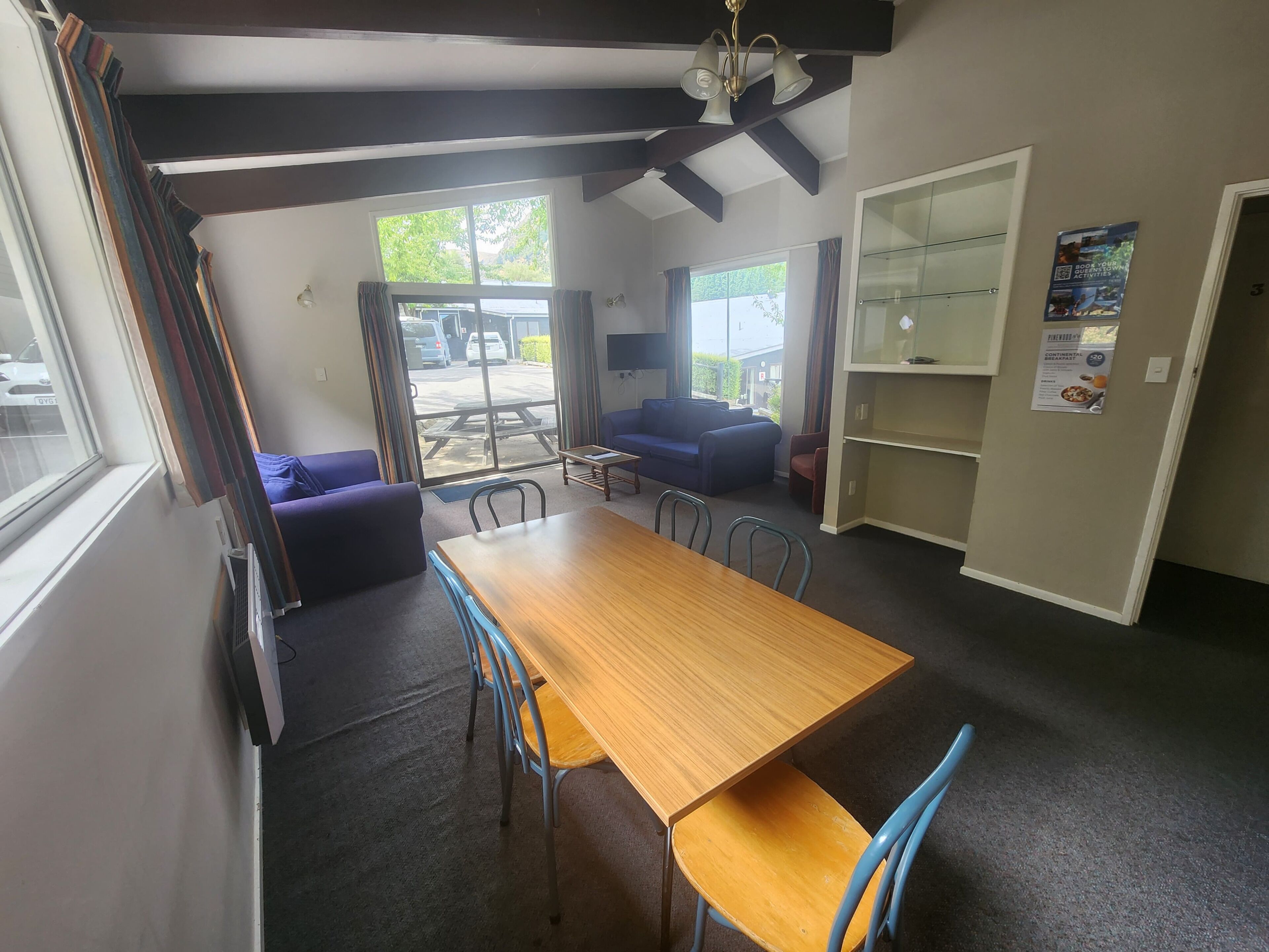 A dining area with a wooden table and blue chairs, a sofa, and a bookshelf.