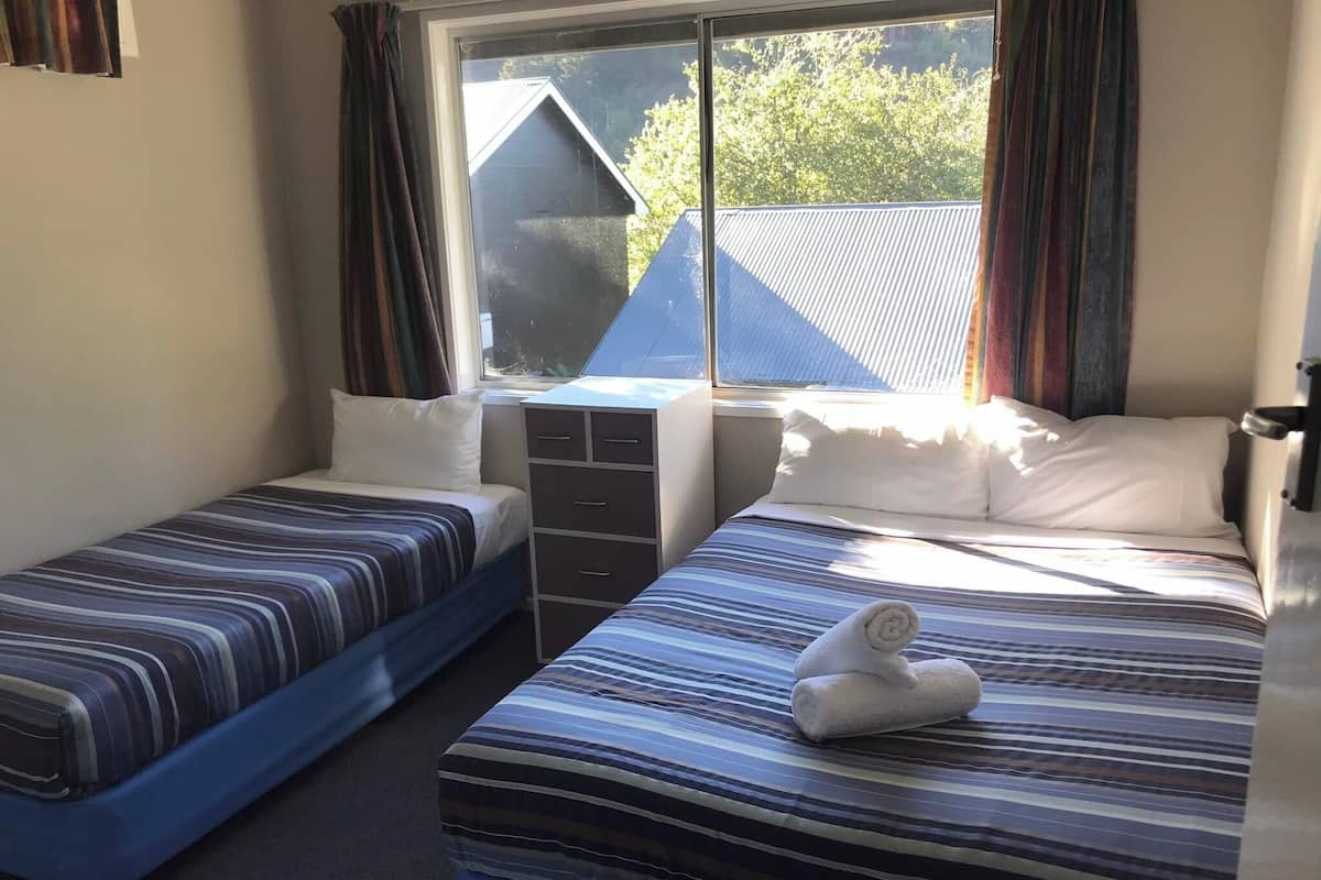 A room with two beds, a dresser, and a window with curtains.