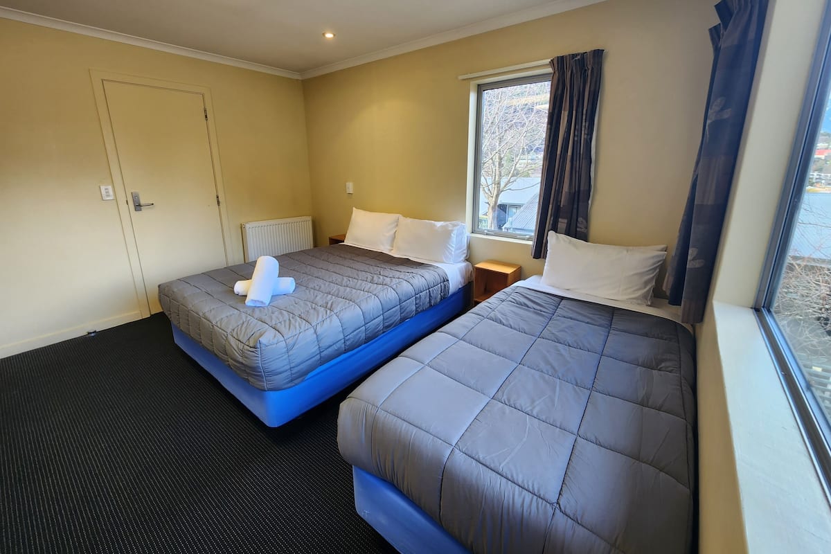 A hotel room with two beds, a window with curtains, a radiator, and a door.