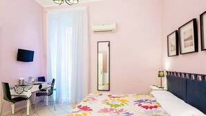 Une chambre avec un lit, un bureau et une chaise. Un téléviseur est fixé au mur et il y a un appareil de climatisation.