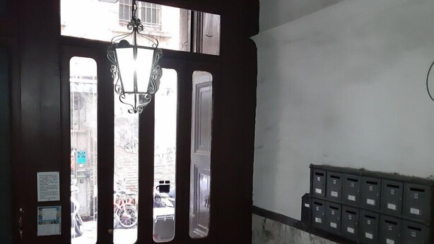 Une pièce avec une porte en bois sombre, un lustre, un sol en marbre et une boîte aux lettres fixée au mur.