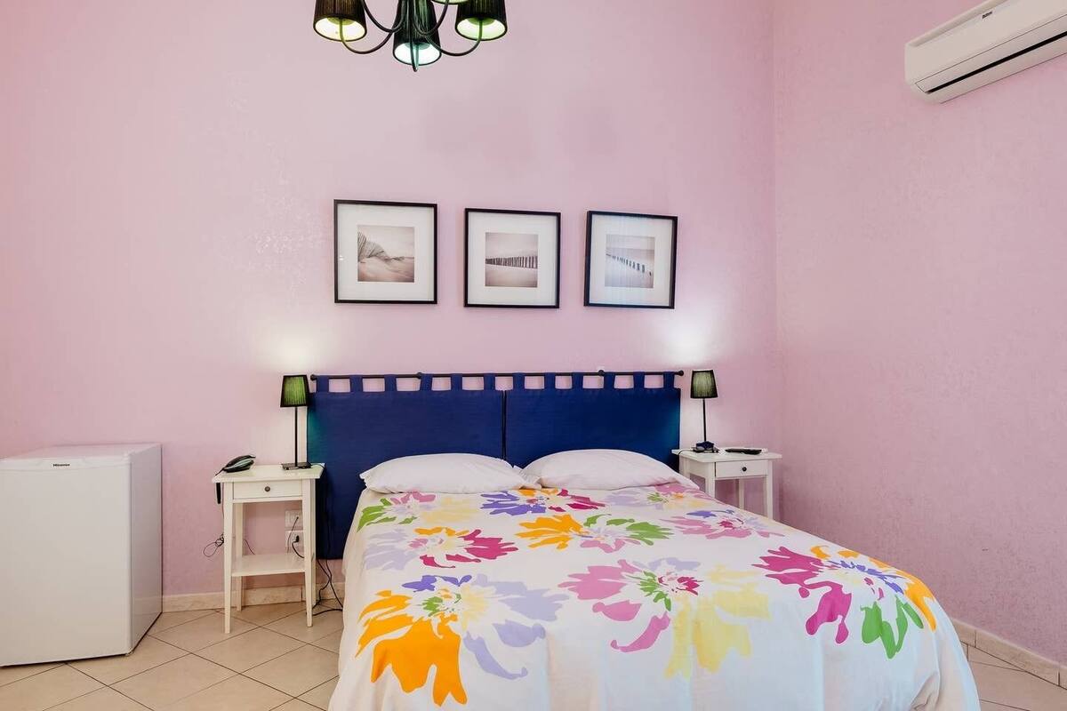 A bedroom with a bed, bedside tables, a desk, a chair, a lamp, and a ceiling light fixture.