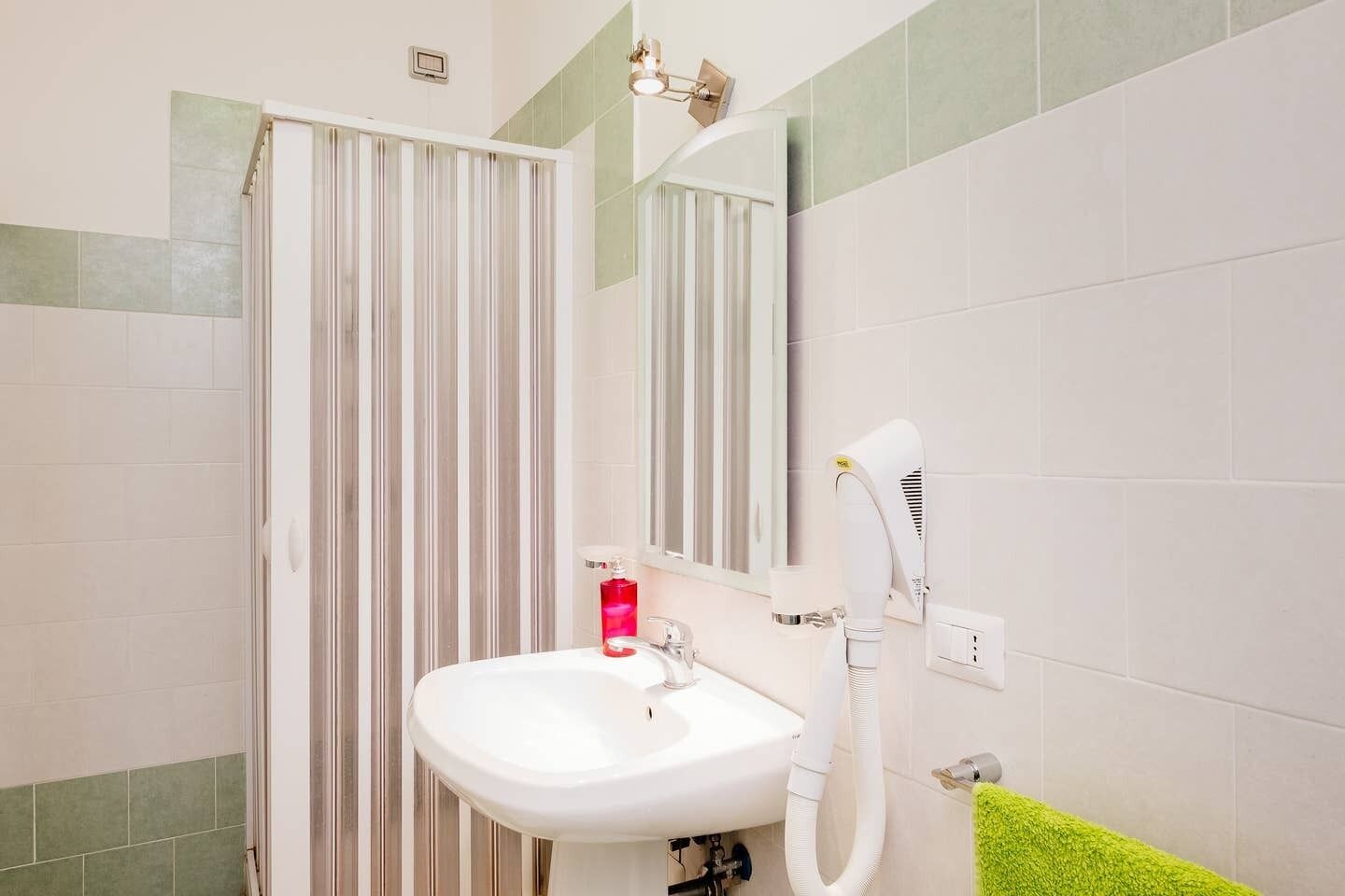 Une salle de bain avec un lavabo blanc, un miroir, un porte-serviettes avec une serviette verte et un rideau de douche.