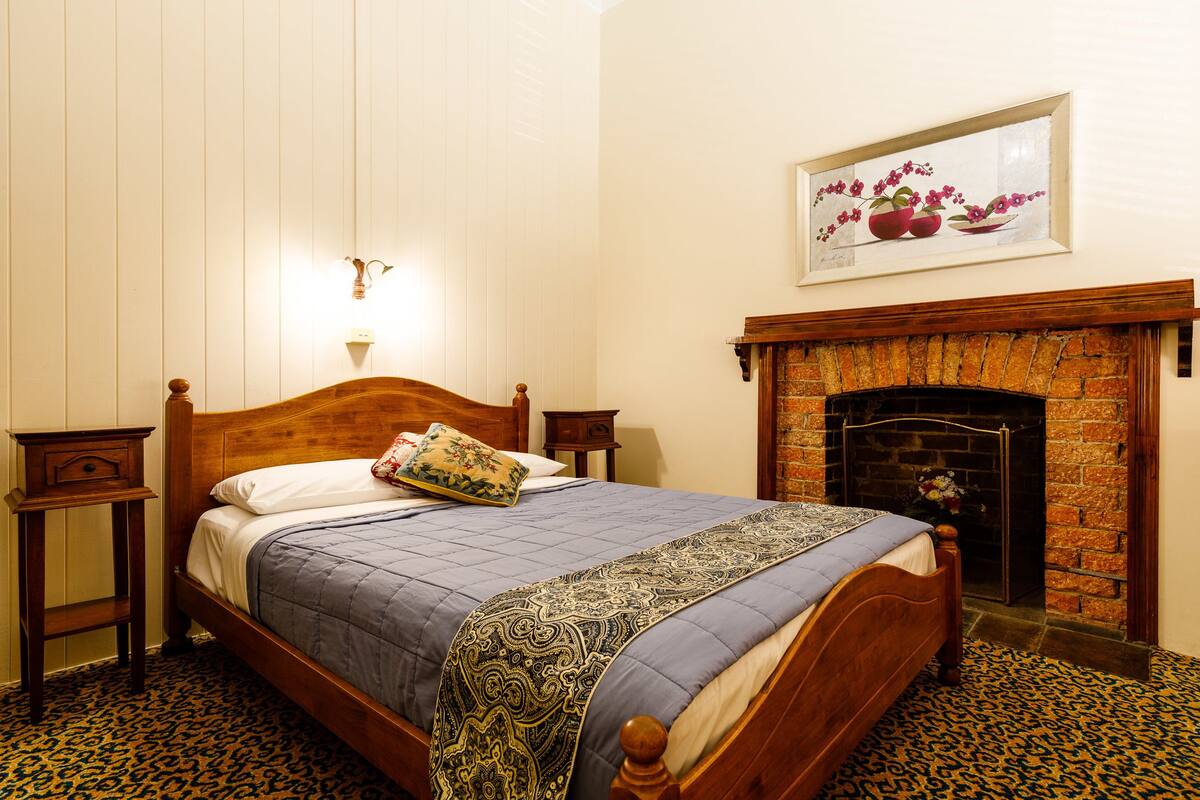 A bedroom with a wooden bed, a brick fireplace, and a framed floral artwork on the wall.