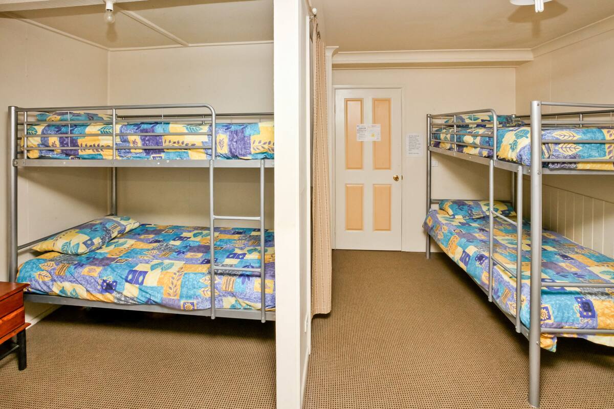 A dormitory room with bunk beds, a door with a sign, and a small wooden table.