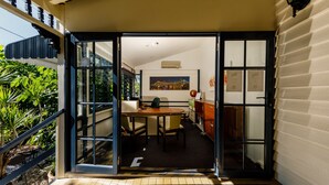 An open door leading to a dining area with a table and chairs, a painting on the wall, and a view of greenery outside. - Bowen Terrace Accommodation (New Farm)