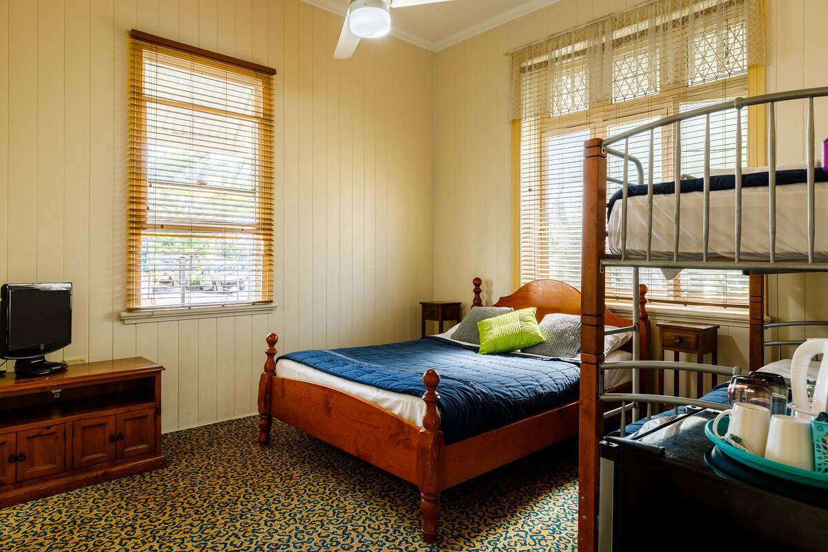A bedroom with a wooden bed, a television on a wooden cabinet, and a bunk bed with a tray table.