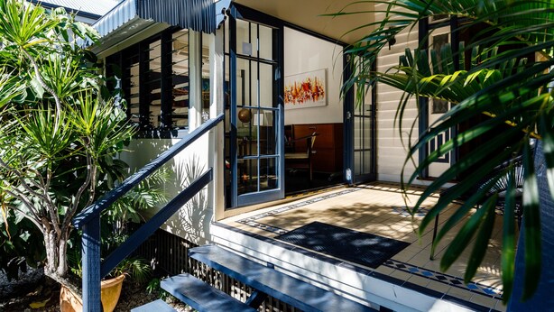 A modern building with a staircase leading to a covered entrance, surrounded by tropical plants. - Bowen Terrace Accommodation (New Farm)