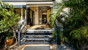 A two-story house with a front porch, a staircase leading to the entrance, and a variety of tropical plants. - Bowen Terrace Accommodation (New Farm)
