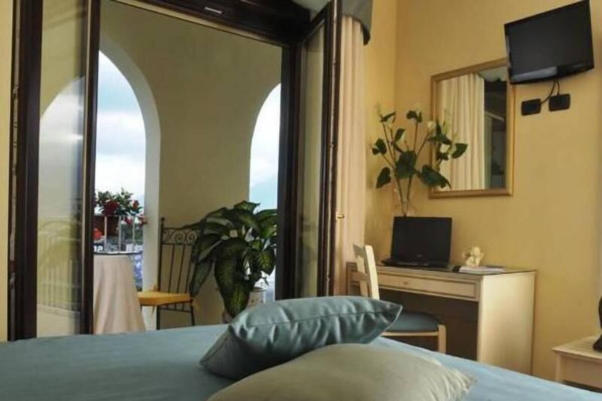 A bedroom with a bed, a desk with a computer, a chair, and a plant.