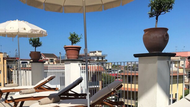 A rooftop terrace with lounge chairs, a large umbrella, and potted plants. - Costa Hotel (Pompei)