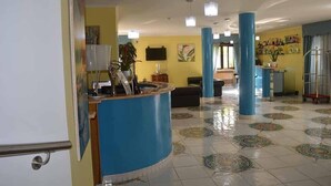 A lobby with a reception desk, blue pillars, a tiled floor, and a bar area with bottles. - Costa Hotel (Pompei)
