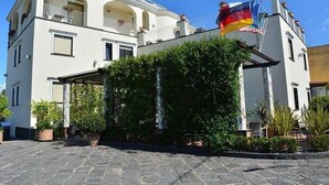 A two-story building with a balcony, potted plants, and multiple flags. - Costa Hotel (Pompei)