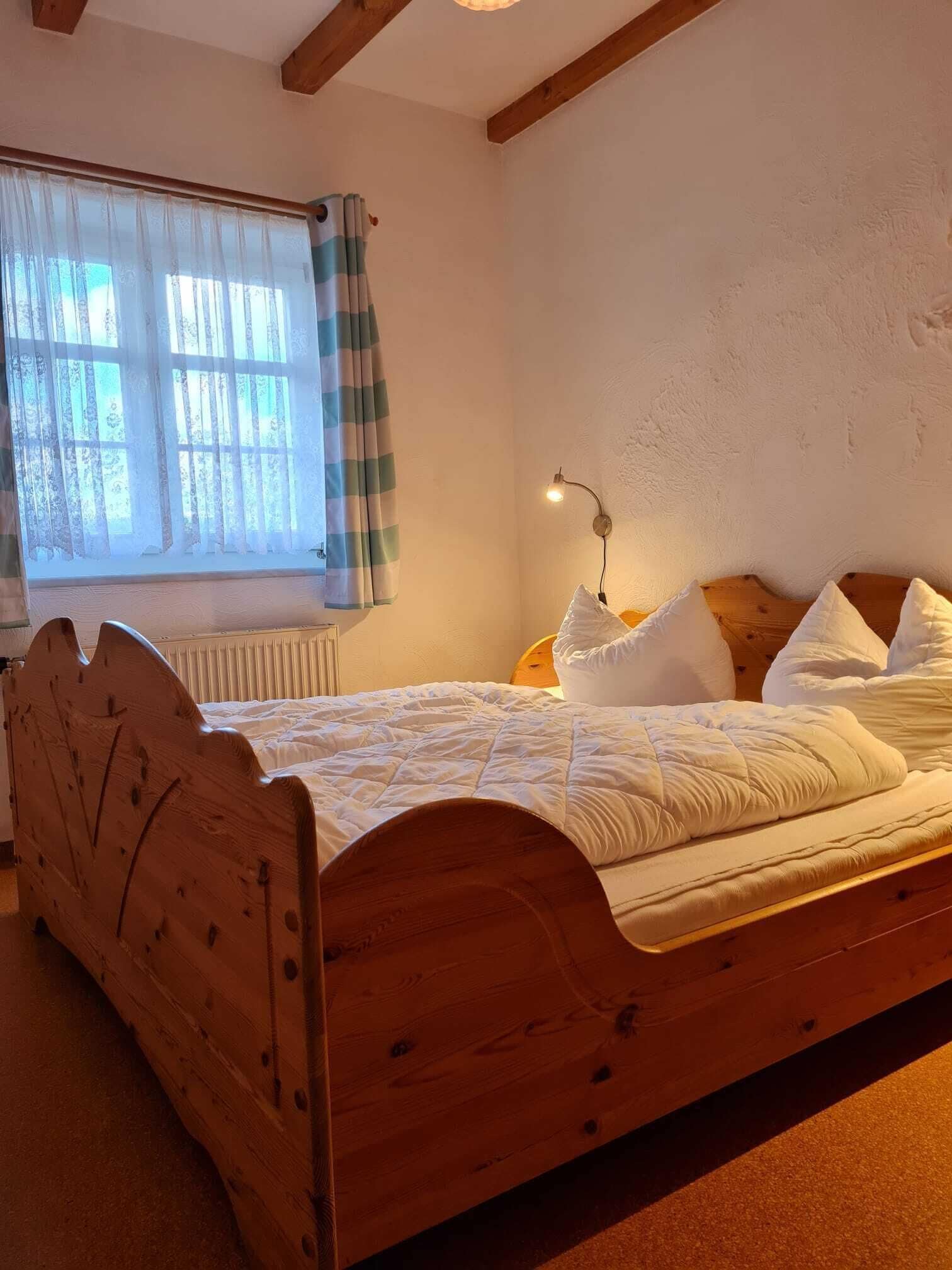 Una cama de madera en una habitación con ventana, un radiador y una lámpara fijada a la pared.