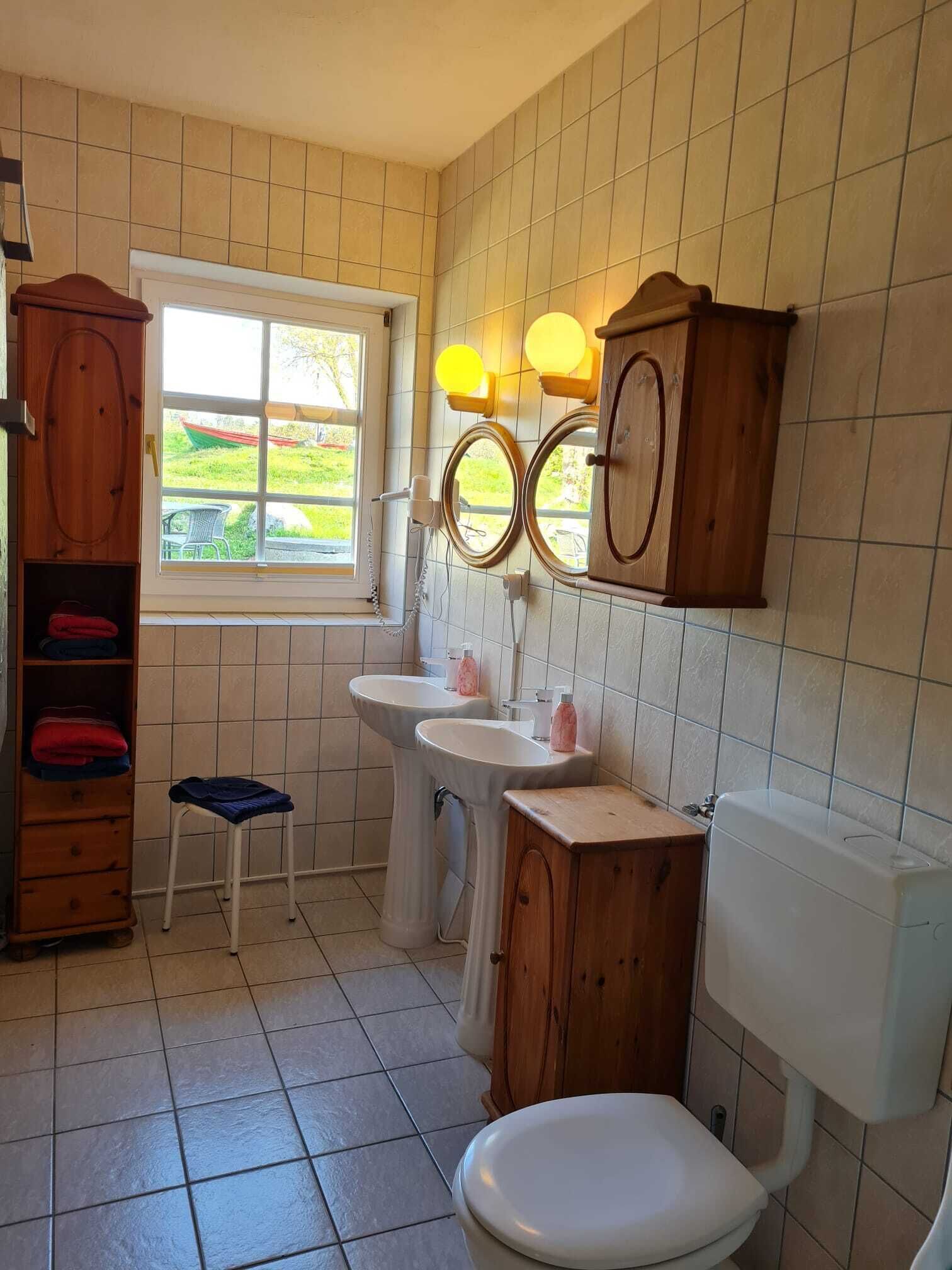 Un baño compacto con dos lavamanos, un inodoro, un armario de madera y una ventana con vistas a zonas verdes.
