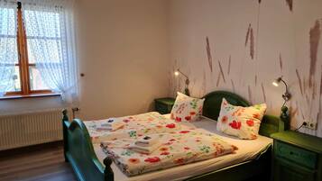 A bedroom with a green bed, floral bedding, a window with sheer curtains, and a wall with a rustic design.