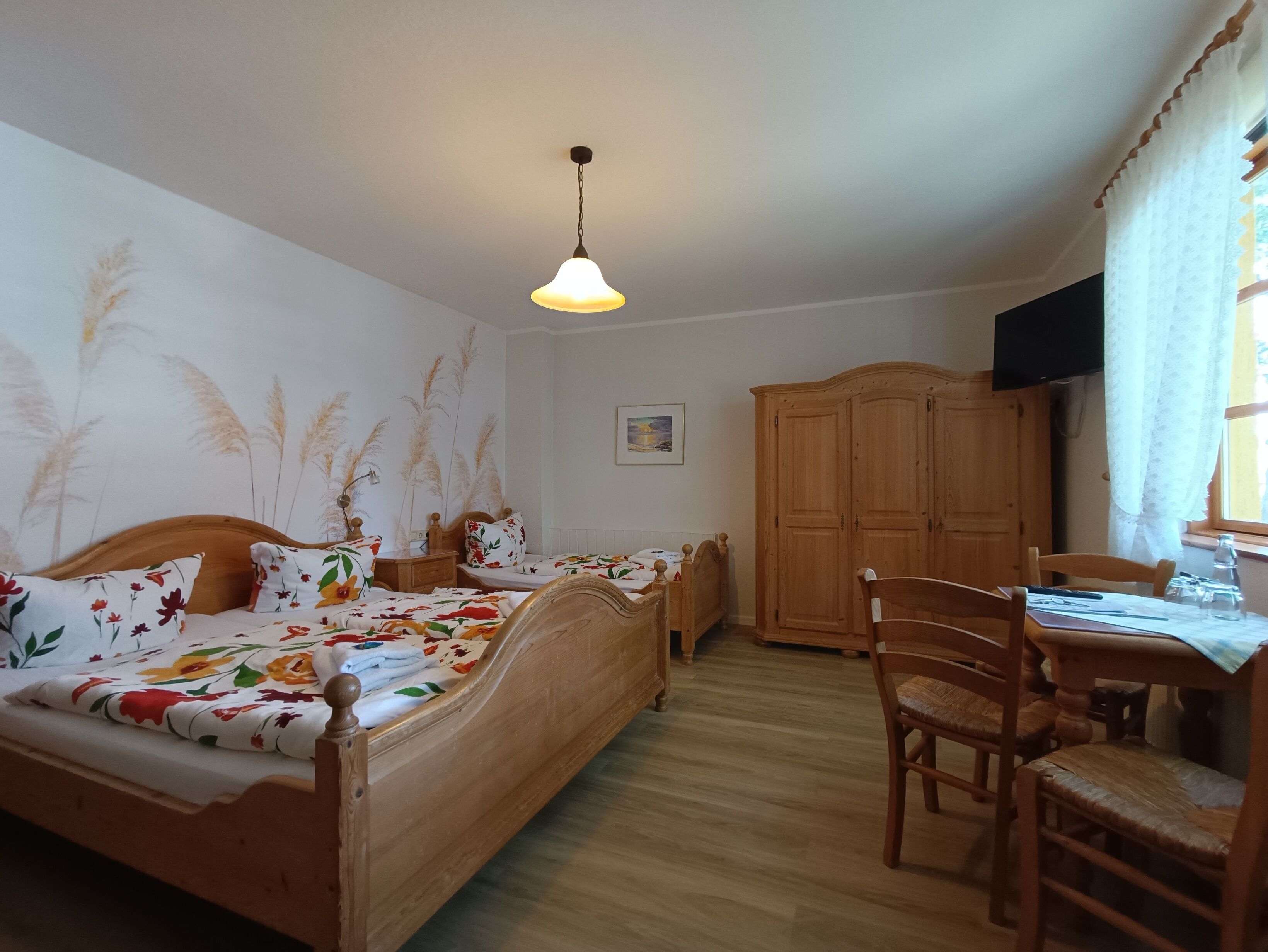 A bedroom with a wooden bed, a desk with a chair, a wardrobe, and a hanging light fixture.