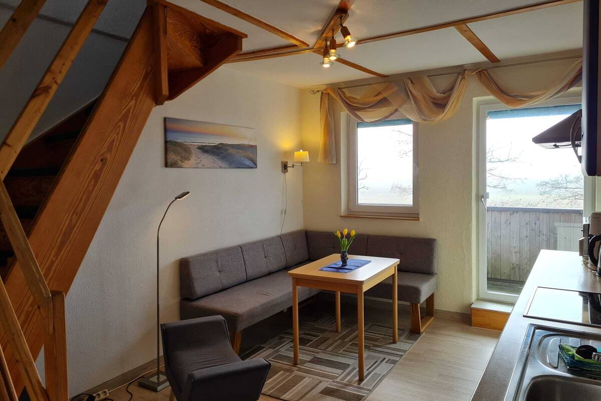 A cozy room with a sofa, a small table, a chair, a painting, a lamp, a window with curtains, and a staircase.