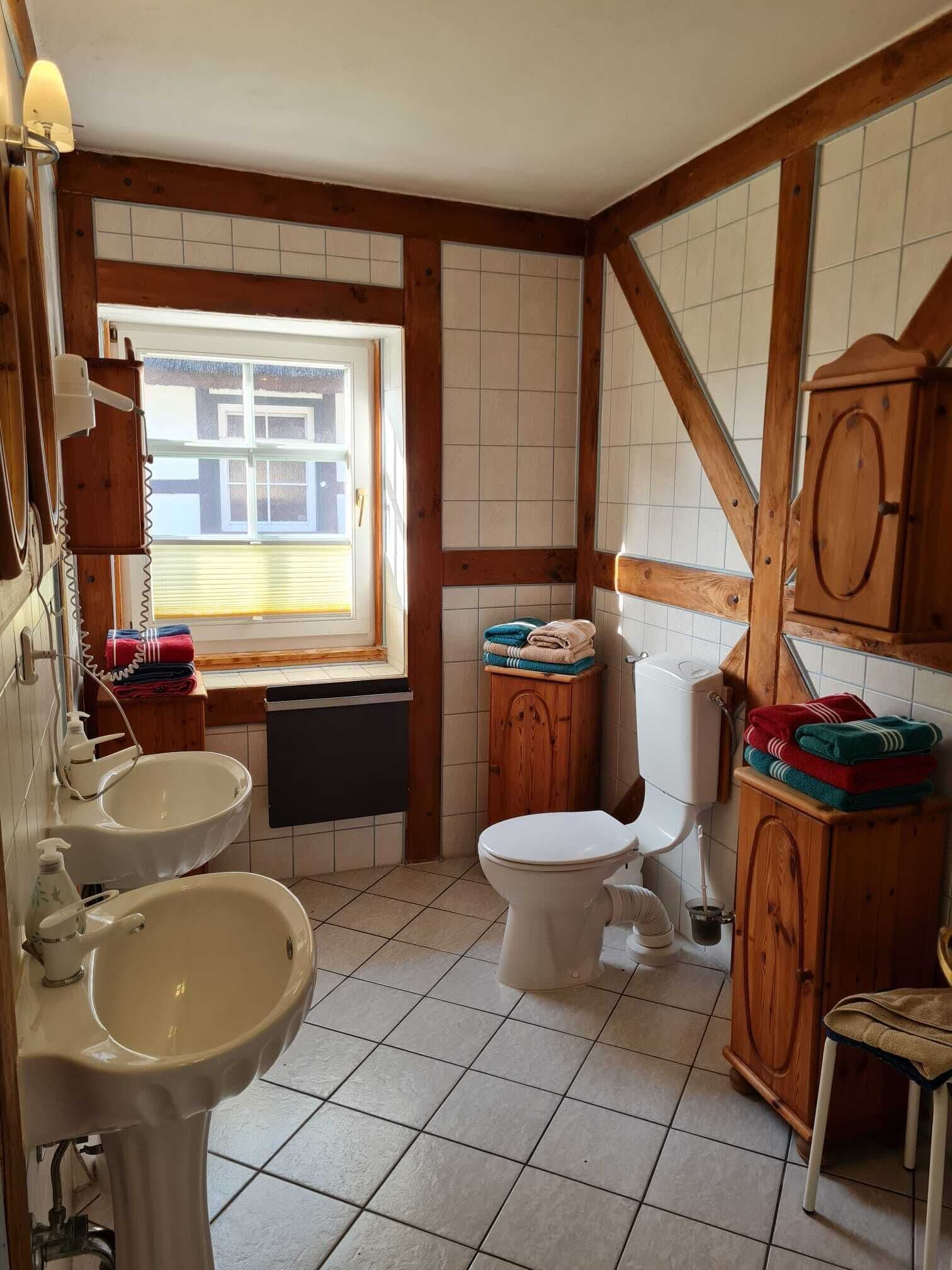 Ein Badezimmer mit Toilette, zwei Waschbecken, einem Fenster und Holzschränken.