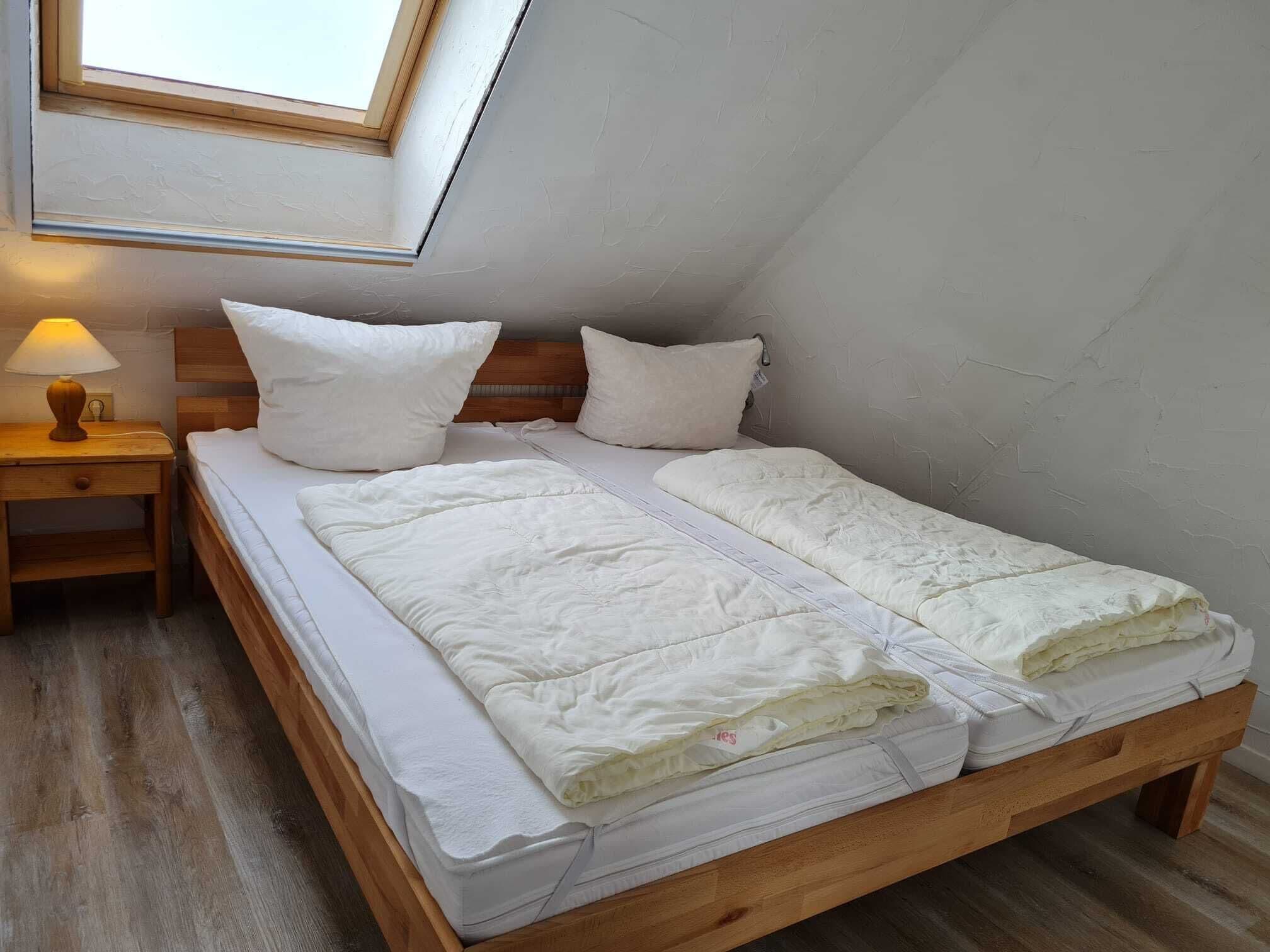 A single bed with a wooden frame, white bedding, and a nightstand with a lamp.
