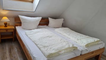A single bed with a wooden frame, white bedding, and a nightstand with a lamp.