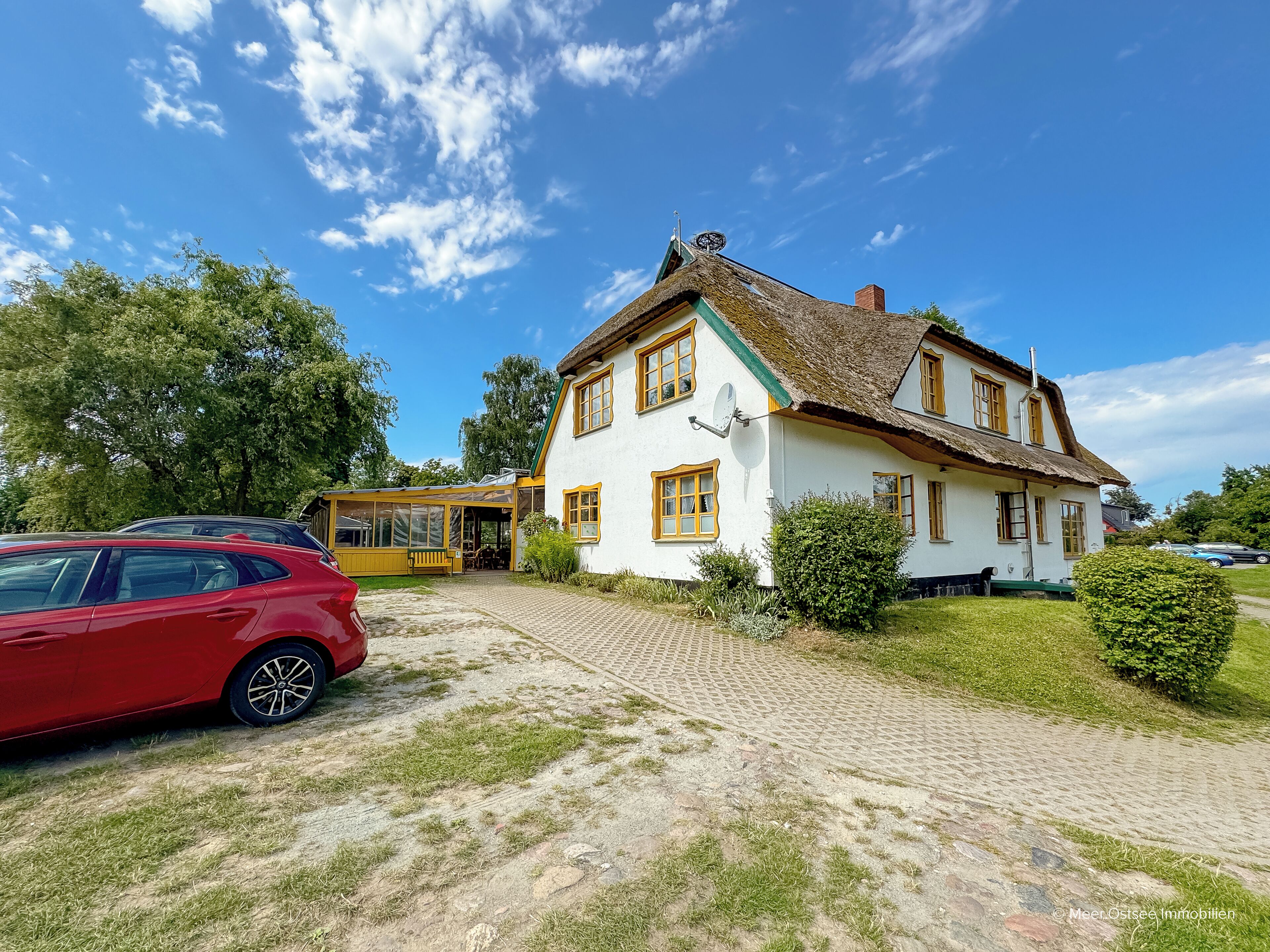 A white house with a thatched roof, a satellite dish, and a paved driveway.