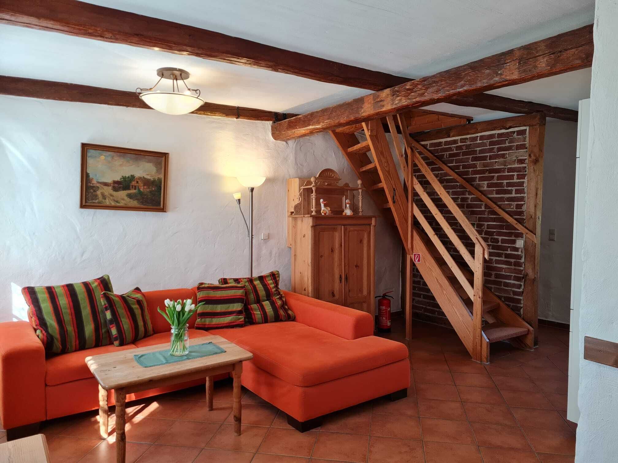 Un salon chaleureux avec un escalier en bois, un ensemble de canapés, une table ornée d’un vase et un tableau accroché au mur.