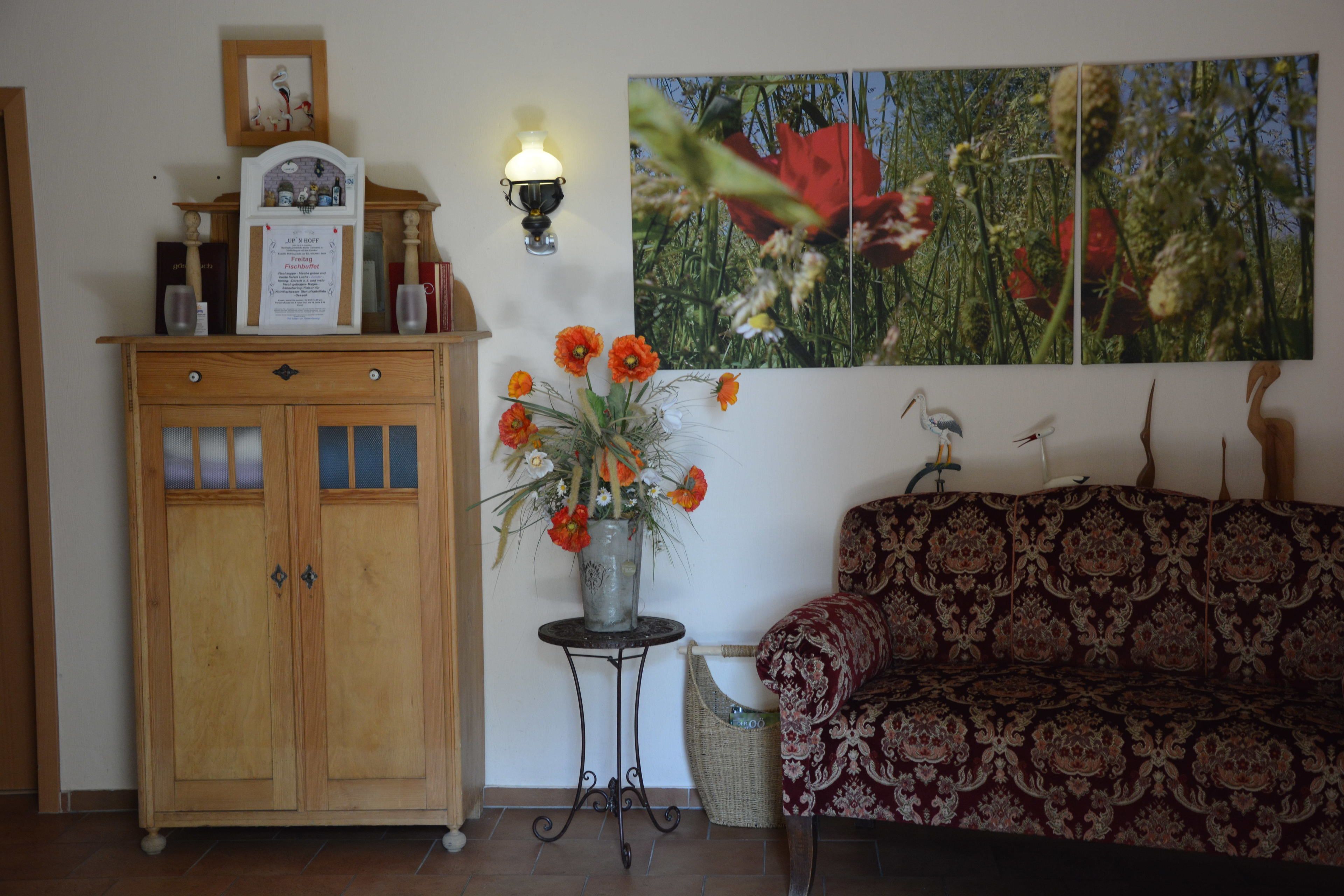 Una habitación con un armario de madera, un jarrón con flores, un sofá estampado y una lámpara de pared.