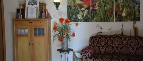 Una habitación con un armario de madera, un jarrón con flores, un sofá estampado y una lámpara de pared.