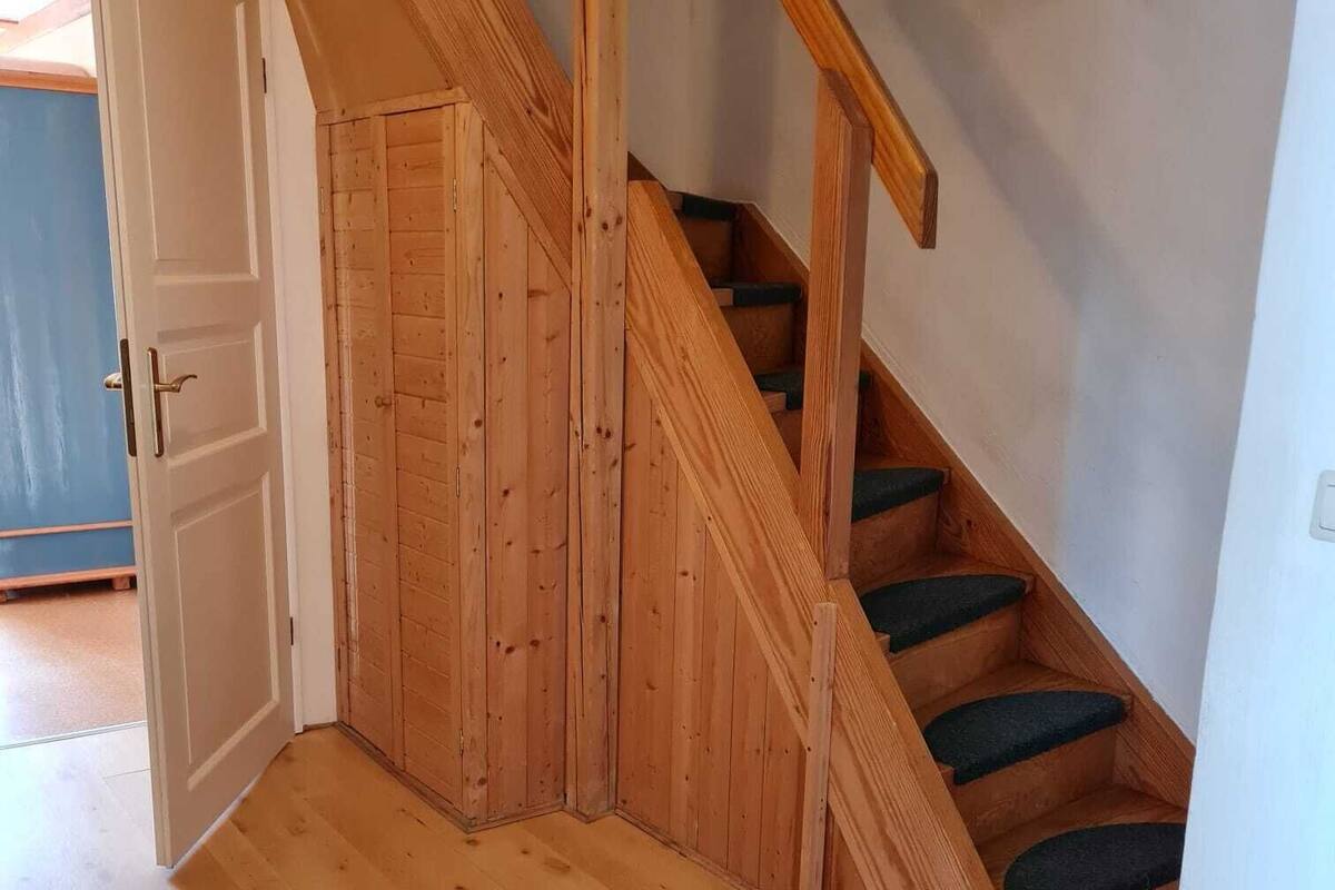 A wooden staircase with green carpeted steps, a white door, and a wooden floor.