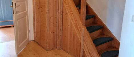 A wooden staircase with green carpeted steps, a white door, and a wooden floor.