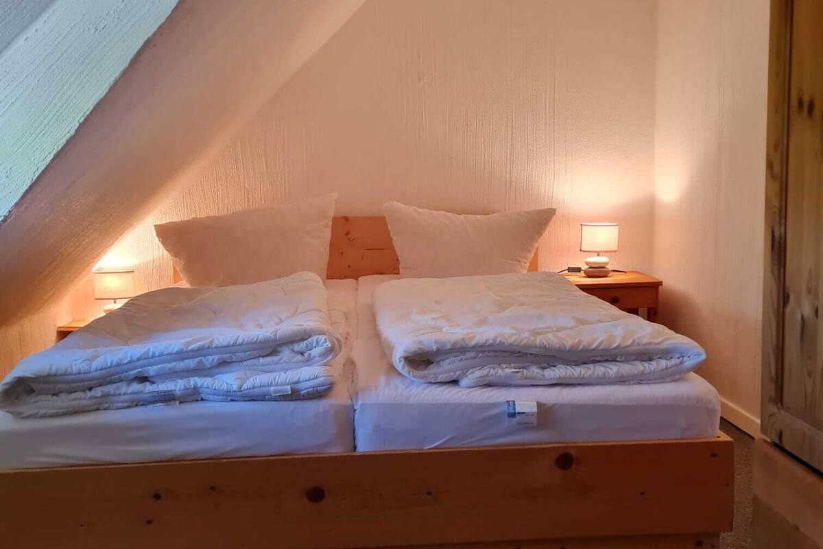 A cozy, single-bed room with a sloped ceiling, wooden headboard, and a bedside table with a lamp.