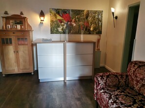 A room with a wooden cabinet, a white dresser, a patterned sofa, and a wall-mounted light fixture. - Reethäuser auf Rügen (Mönchgut-Granitz)