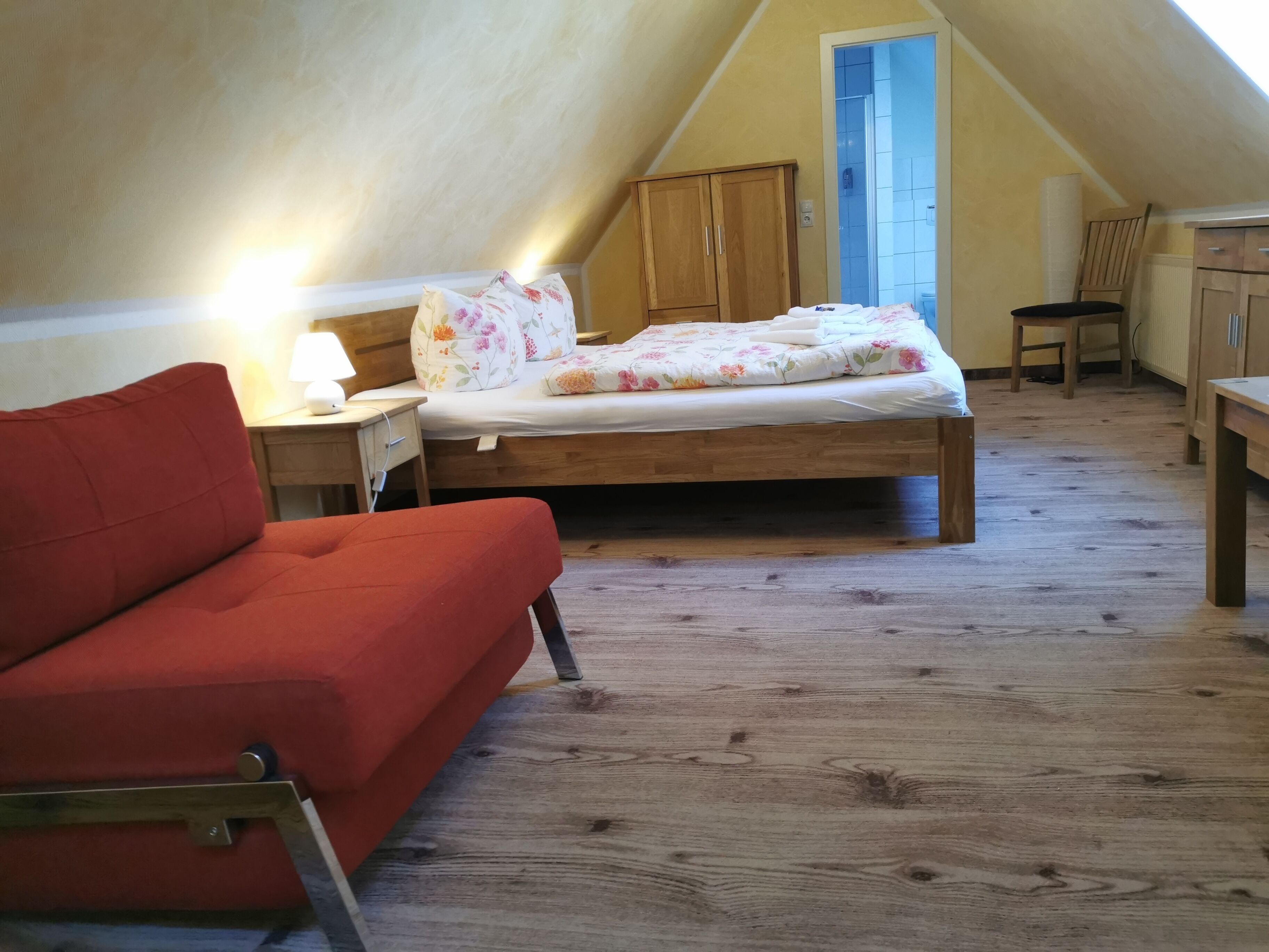 Ein gemütliches Schlafzimmer im Dachgeschoss mit einem Holzbett, einem roten Sofa und einem kleinen Schreibtisch.