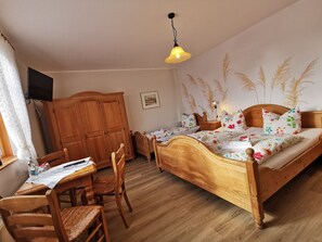 A bedroom with a wooden bed, a desk with chairs, a wardrobe, and a television on the wall. - Reethäuser auf Rügen (Mönchgut-Granitz)