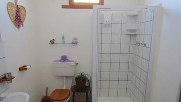 Une salle de bain équipée de toilettes, d’un lavabo, d’une douche et d’une petite étagère où sont rangés les articles de toilette.