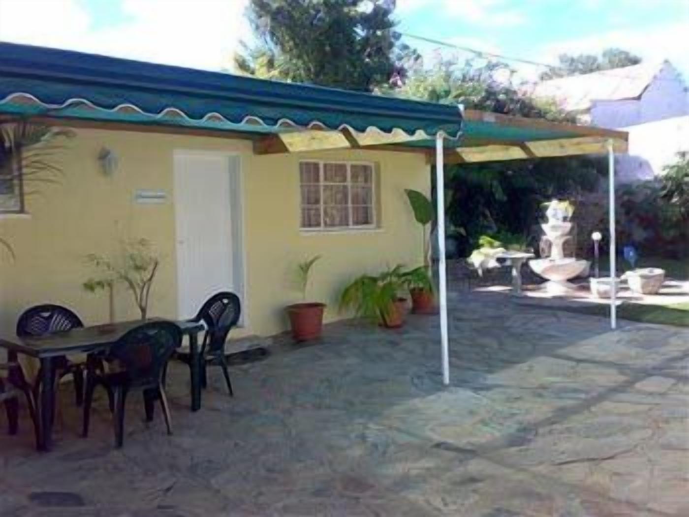 A small building with a covered patio area, a table with chairs, and potted plants.