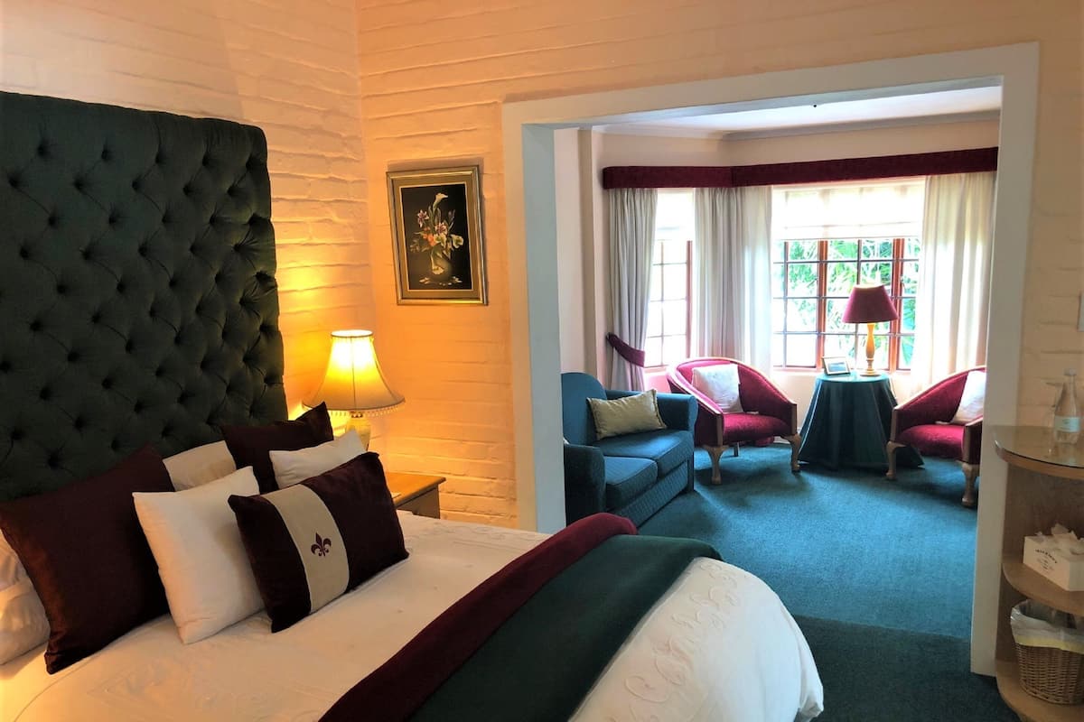 A hotel room with a large bed, a sitting area with two armchairs, a small table, and a window with curtains.