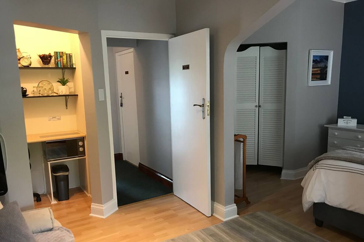 A bedroom with a bed, a bedside table, a dresser, a closet, and a hallway leading to a bathroom.