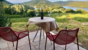 A table with a bottle and two glasses, set on a patio with chairs, overlooking a lake and hills. - Liscia Country Relais (Luras)