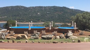 A pool area with two sun loungers and umbrellas, surrounded by rocks and a view of a lake and mountains. - Liscia Country Relais (Luras)
