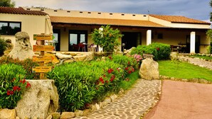 A building with a tiled roof, a stone pathway, and a signpost with directions. - Liscia Country Relais (Luras)