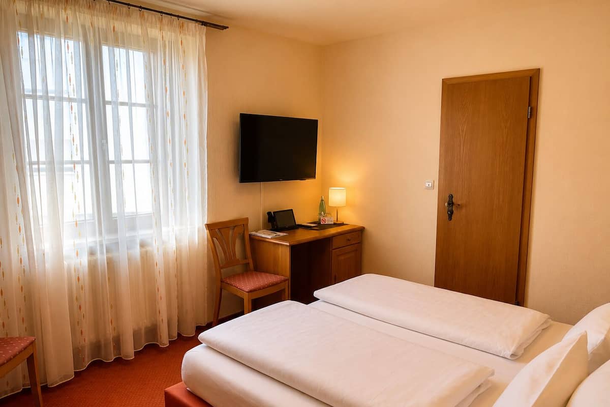 A hotel room with a bed, a desk with a computer, a chair, a TV, and a door.