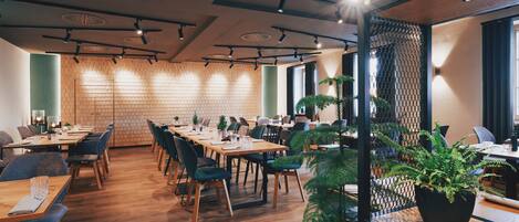 A modern dining area with wooden tables and chairs, a brick wall, and potted plants.